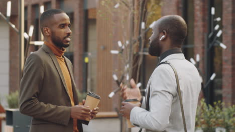 two black businessmen holding coffee and talking on street