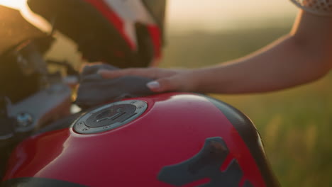 un primer plano de una mano limpiando suavemente el tanque de combustible rojo de una motocicleta usando un paño