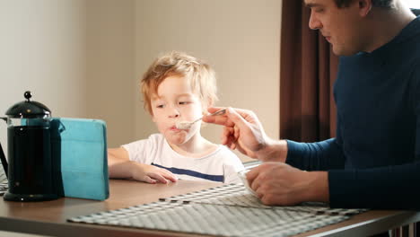 Father-feeding-his-son-while-he-watching-cartoons-on-pad