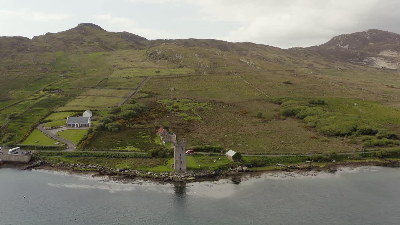 Aerial pullback reveals Grace O'Malley's Towerhouse on calm peaceful irish shore, achill island