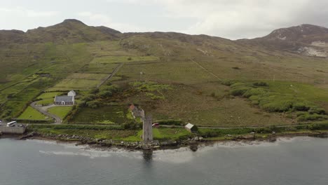 aerial pullback reveals grace o'malley's towerhouse on calm peaceful irish shore, achill island