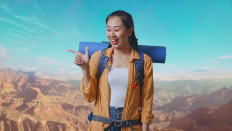 Asian Female Hiker With Mountaineering Backpack Smiling And Pointing To Side While Traveling At The Top Of Mountain