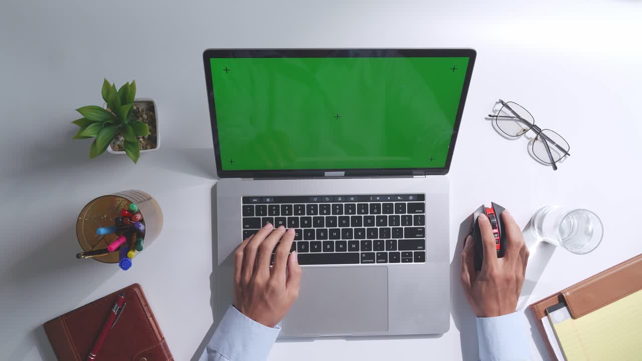 vista de arriba hacia abajo de una computadora portátil con pantalla verde simulada pantalla chromakey en un escritorio de oficina de madera al lado de la libreta con bolígrafos, gafas y un vaso de agua.