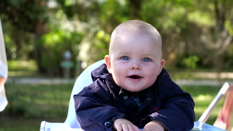 portrait shot of cute young baby with blue eyes smiling into camera outside in park,close up