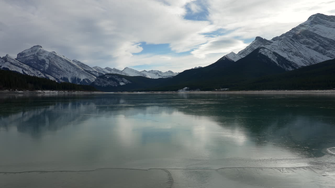 Panning shot of a mountain lake starting to freeze in the winter.