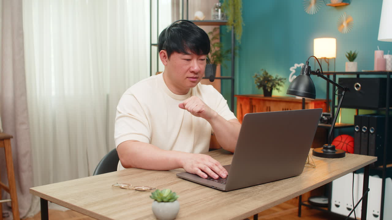Asian man on laptop headset video call giving live support with calm tone online customer service