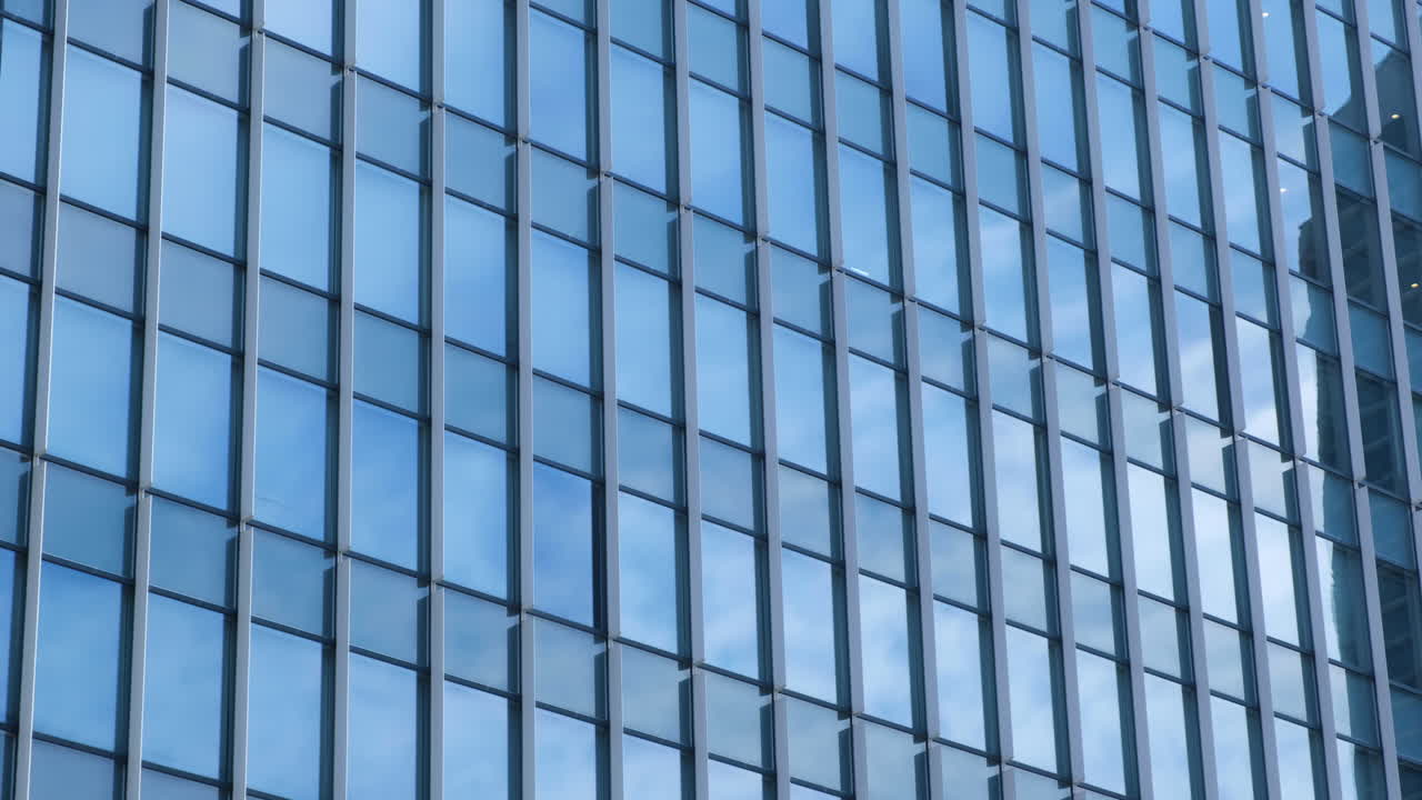 Paredes modernas de vidrio y acero con reflejos de edificios y cielo azul.