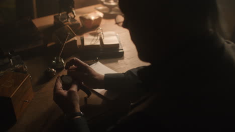 older passionate man evaluates an old watch in his office at night