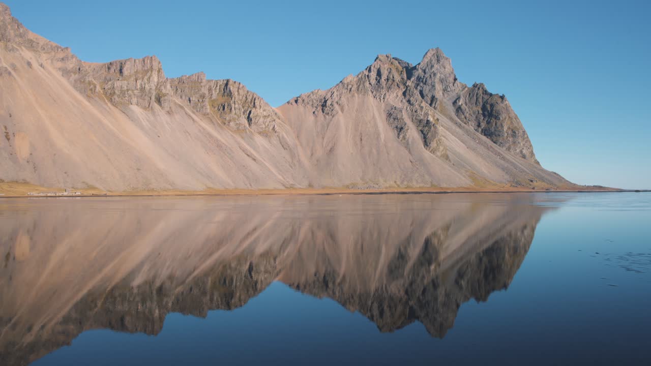 Jagged Vestrahorn mountain ridge reflected in clear blue sea water