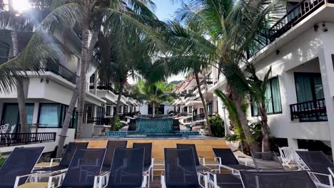 tropical hotel resort featuring empty sunbeds, lush palm trees, and a sunny atmosphere perfect for relaxation.