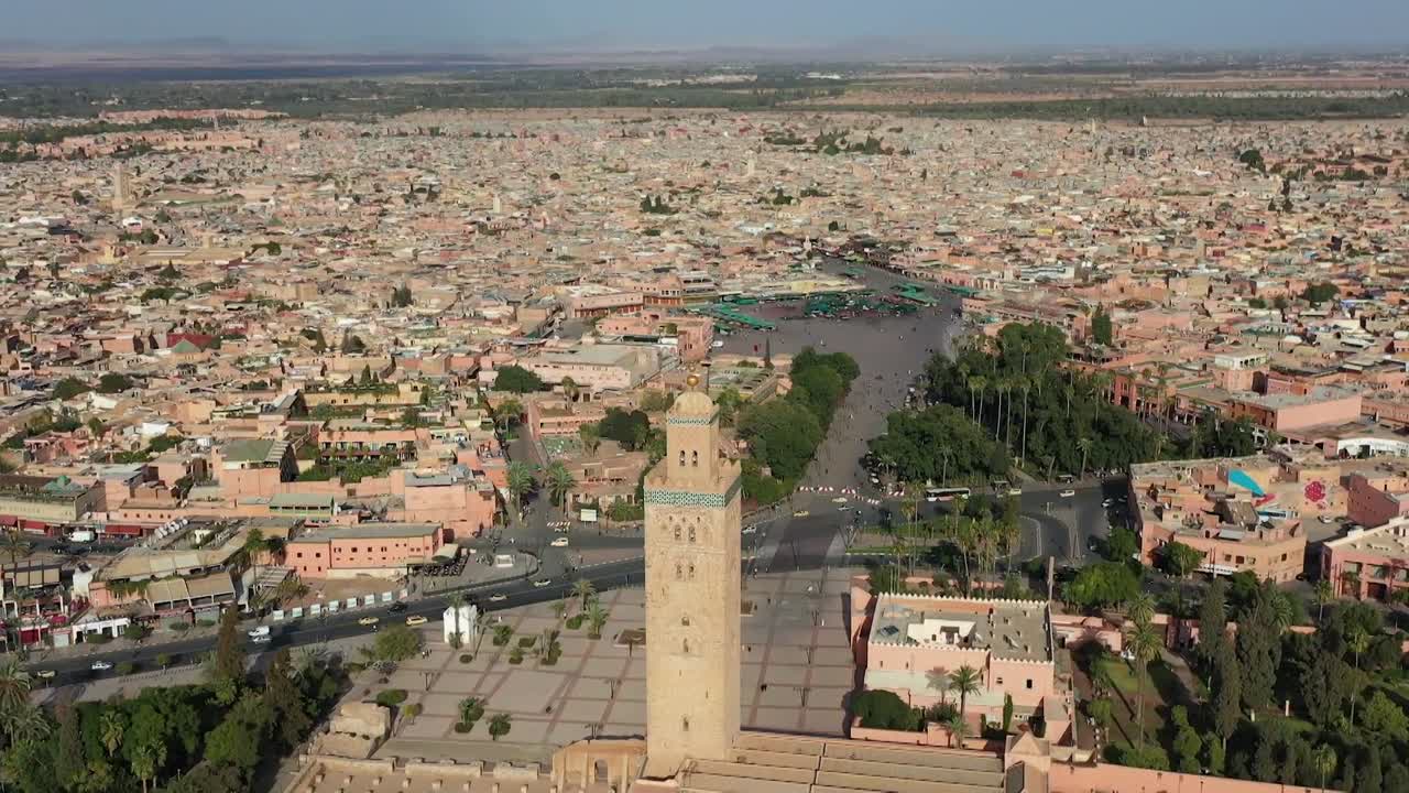 Tarihi Kutubiye Minaresi'ni gösteren görkemli drone çekimi. Genişleyen kırmızı tonlu Medine'yi, uzaktaki Cemaa el-Fna Meydanı'nı ve merkezi Marakeş'in geleneksel mimarisini yakalar.