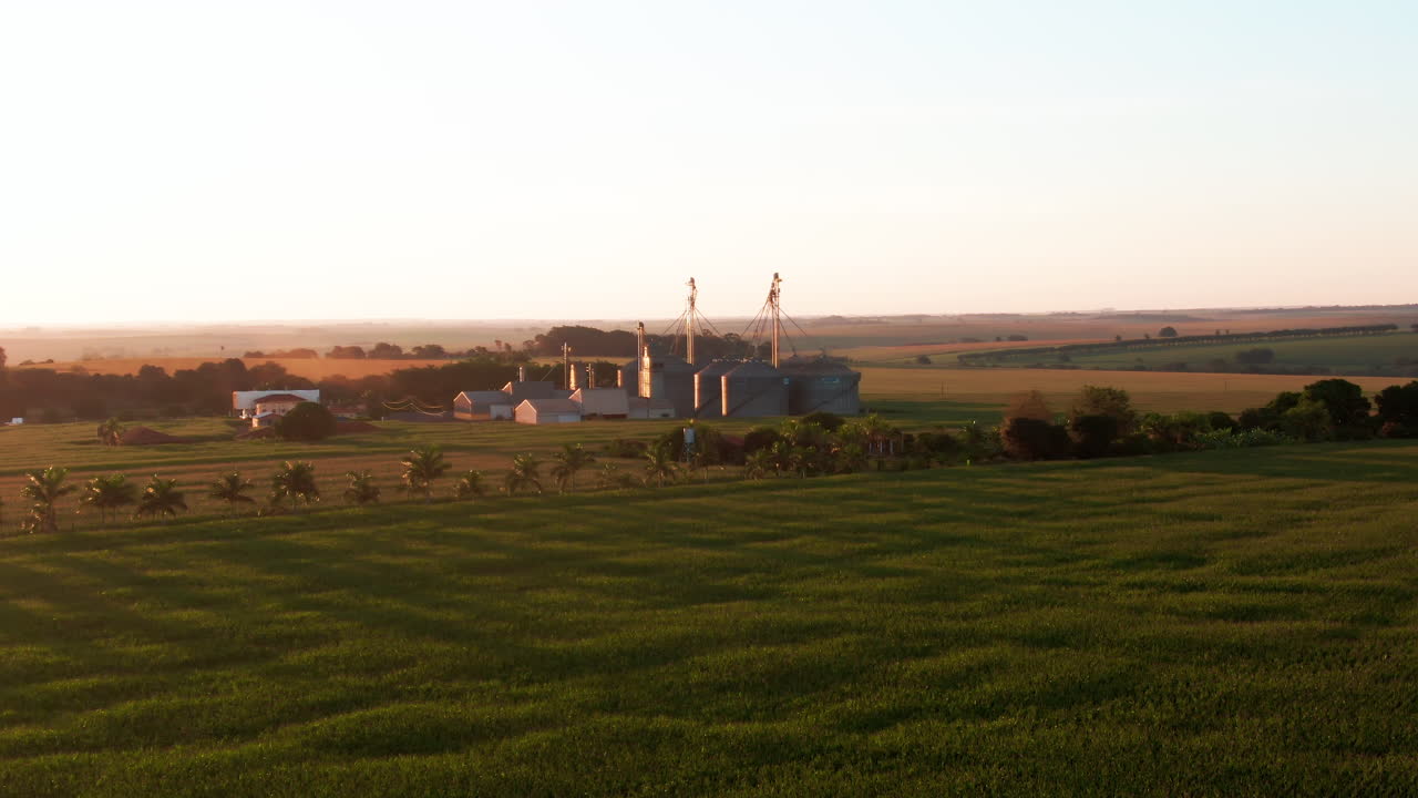 Drone aerial landscape afternoon sunset across countryside crops plantations valley with grain silo industrial factory facility with tanks in Brazil South America infrastructure agriculture wheat