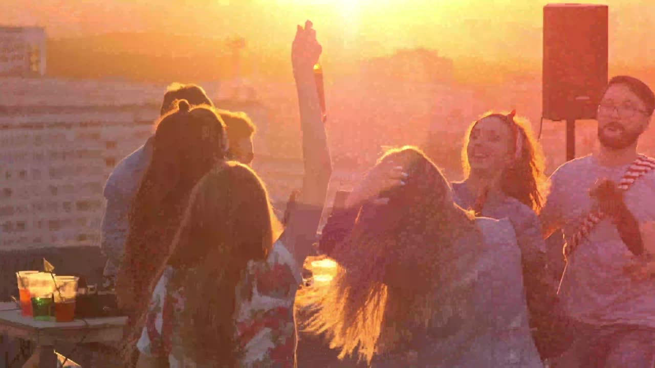 Vennegruppe danser og fester på en tagterrasse ved solnedgang