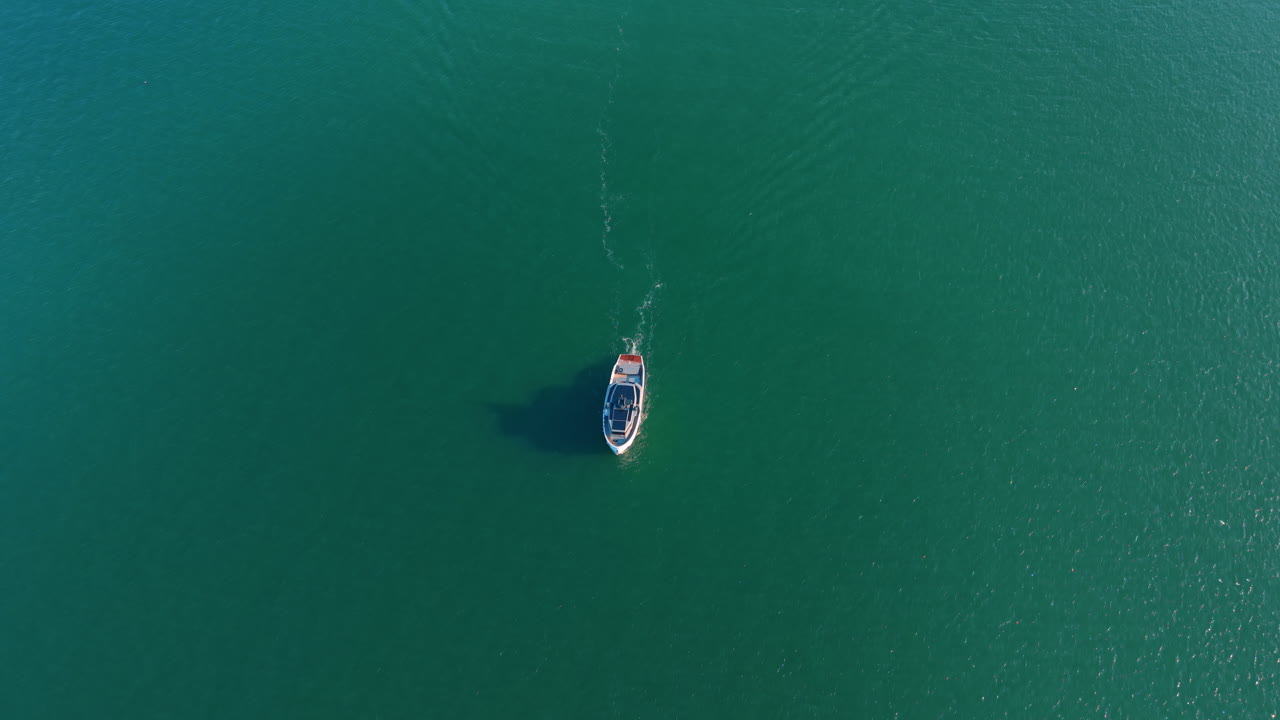 Vista dall'alto minimalista di una barca su acqua turchese. Scatto aereo verticale di un singolo motoscafo che si muove in acqua marina calma e verde con spazio per il testo.