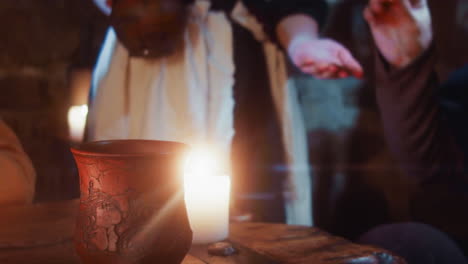 woman servant pours wine into guest clay mug in tavern. medieval maid in white apron fills client cup with alcohol in pub closeup. dark ages inn service