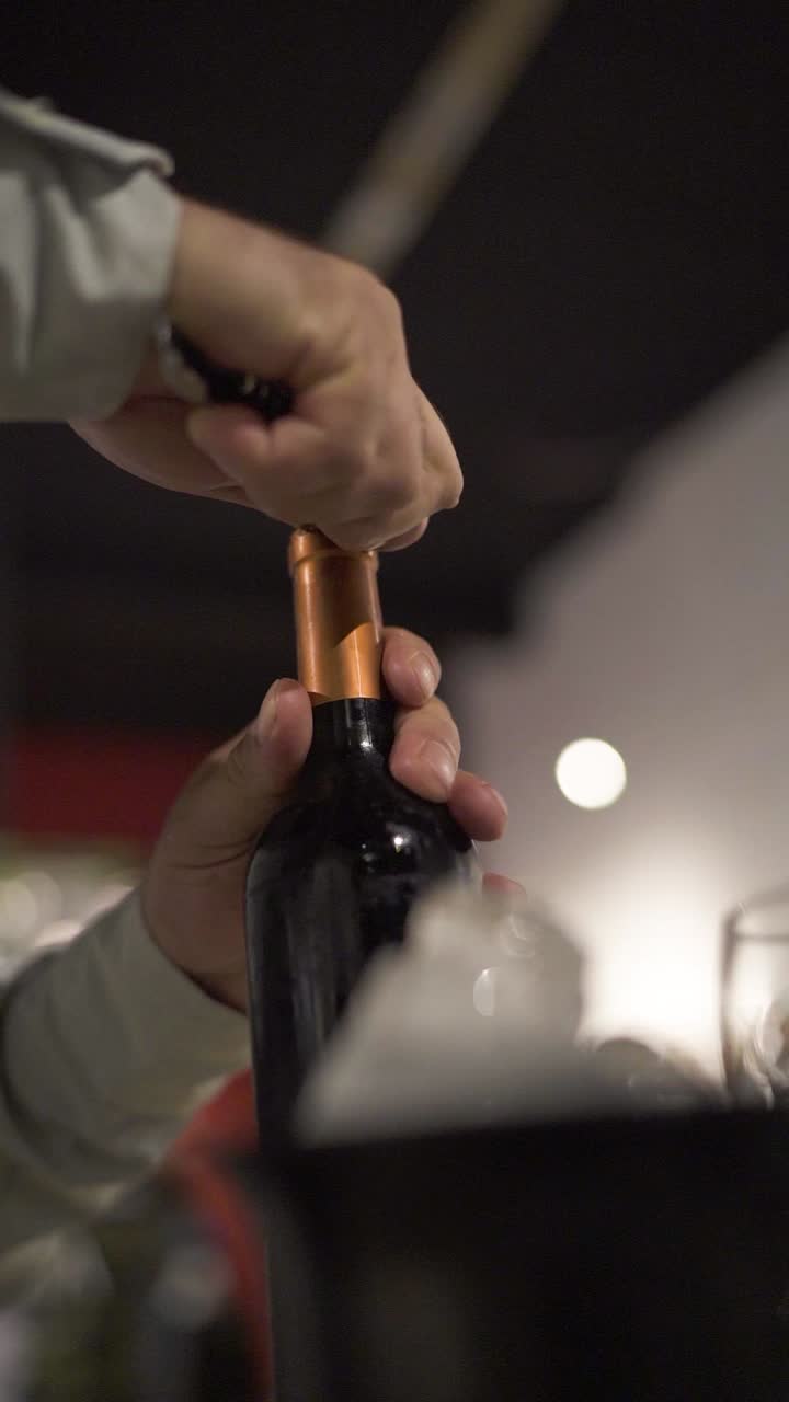 Primo piano di un uomo che rimuove il sigillo di sicurezza da una bottiglia di vino durante una cena elegante.