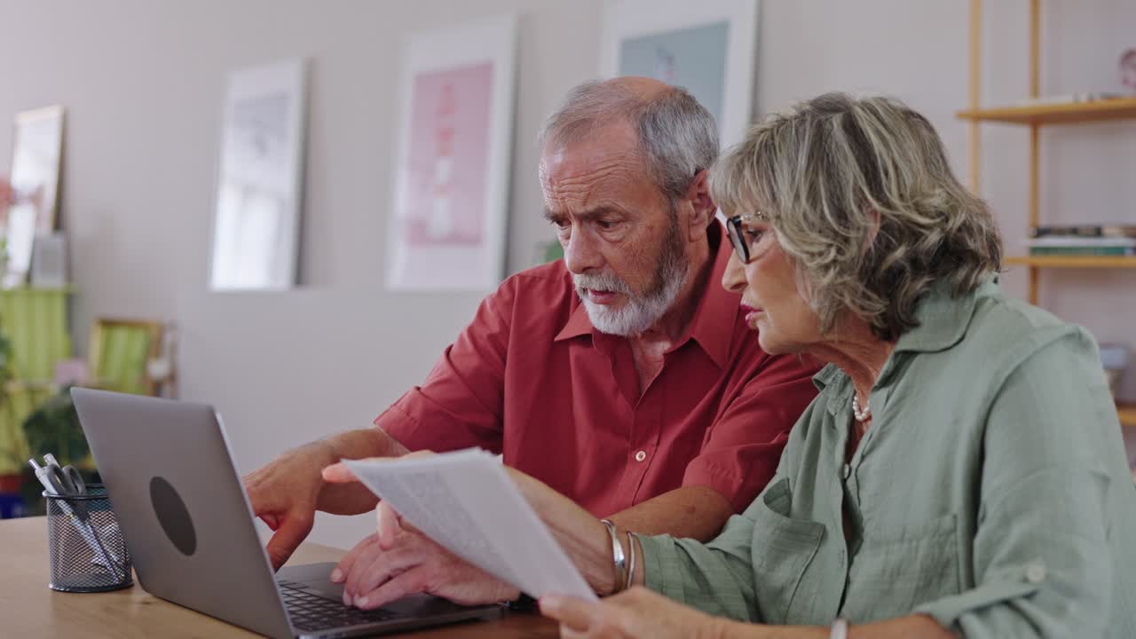 Casal de idosos gerenciando as finanças em casa com um laptop