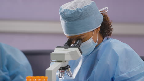 female lab worker wearing ppe analysing slide under microscope