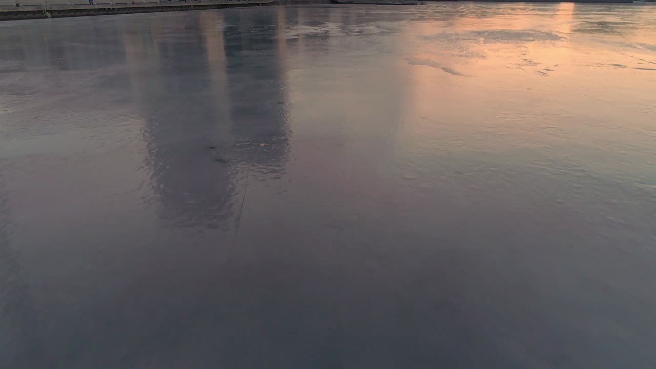 Drone shot flying over ice, frozen bay and camera pan up to modern apartment buildings in Stockholm, Sweden. View of contemporary residential district at dusk