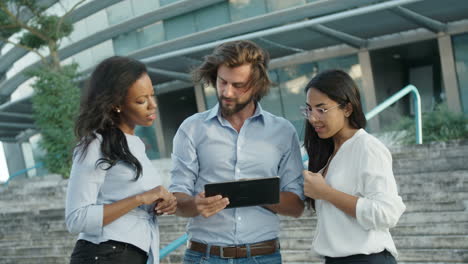 serious tall bearded man holding portable computer, showing something in a table to female colleagues