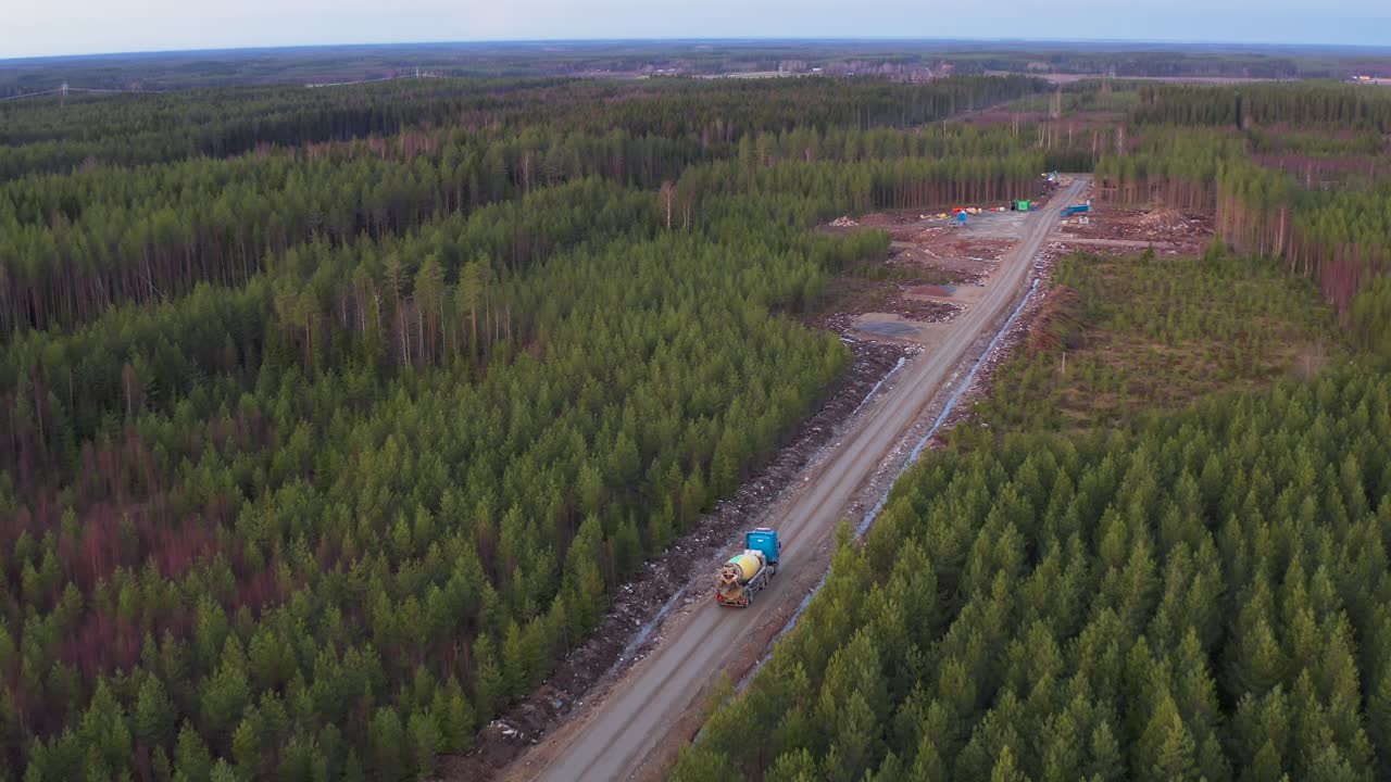 vista aérea de un camión hormigonera conduciendo a través del bosque hacia el sitio de construcción