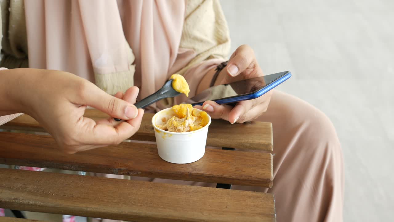 Women eating ice cream and using smart phone while sited ,