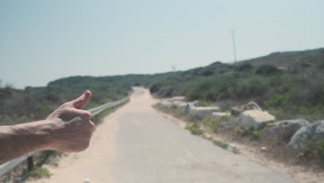 closeup of hitchiker's hand trying to catch a ride home on hot road