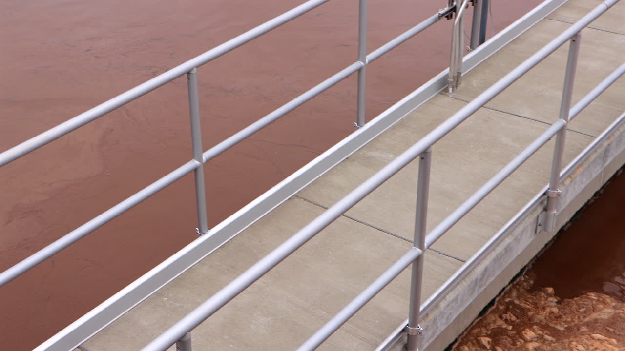 Waste water is being gently agitated in an aeration basin. Foam is forming on top of the brown water