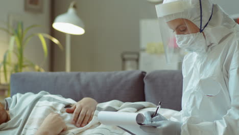 Hombre-Enfermo-Que-Recibe-Una-Receta-Del-Médico-Con-Traje-Protector-En-Casa