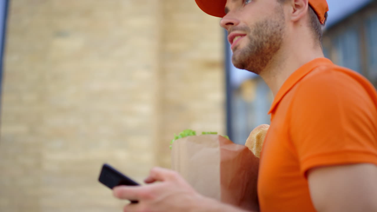 mensajero con bolsa de papel y teléfono móvil al aire libre. hombre entregando comida.