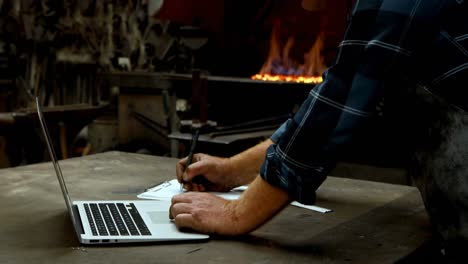schmied schreibt auf dem clipboard, während er einen laptop 4k verwendet