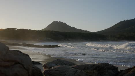 Meereswellen-Kommen-Bei-Sonnenuntergang-Auf-Den-Strand-Zu-Kriechen,-Mit-Bergen-Im-Hintergrund