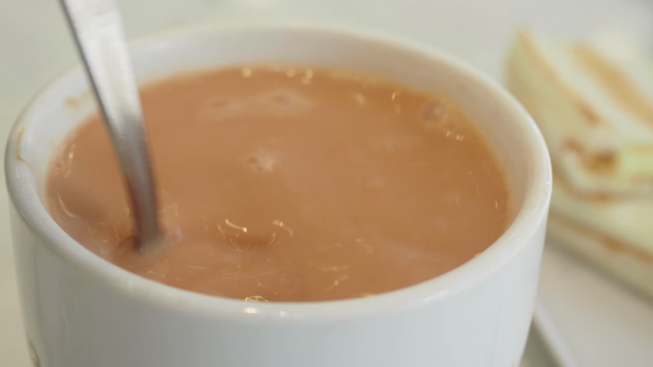 Una tazza di tè al latte con un cucchiaio e un panino
