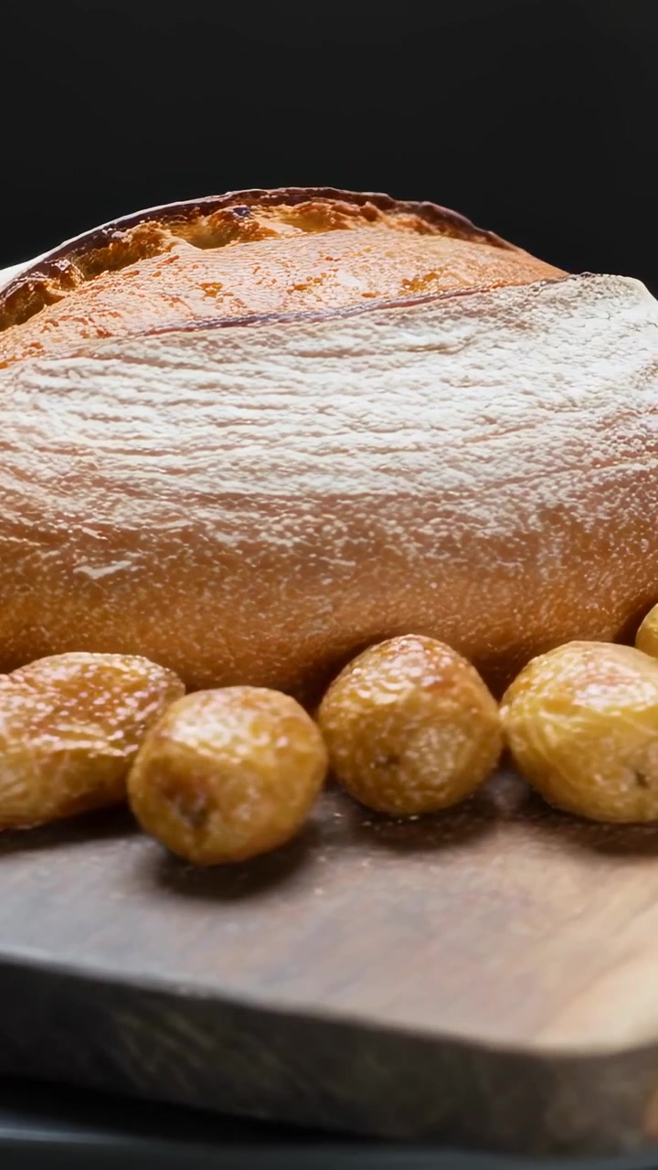 Vertical video: Shifting camera zooming, emphasizing crust on loaf and roasted potatoes on board