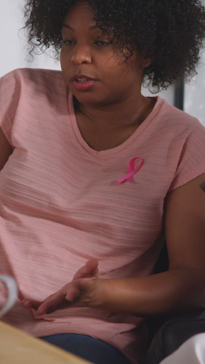video vertical de una mujer adulta que lleva una cinta rosa de concienciación sobre el cáncer de mama reuniéndose y hablando en un grupo de apoyo terapéutico para pacientes con tratamiento de cáncer con un consejero