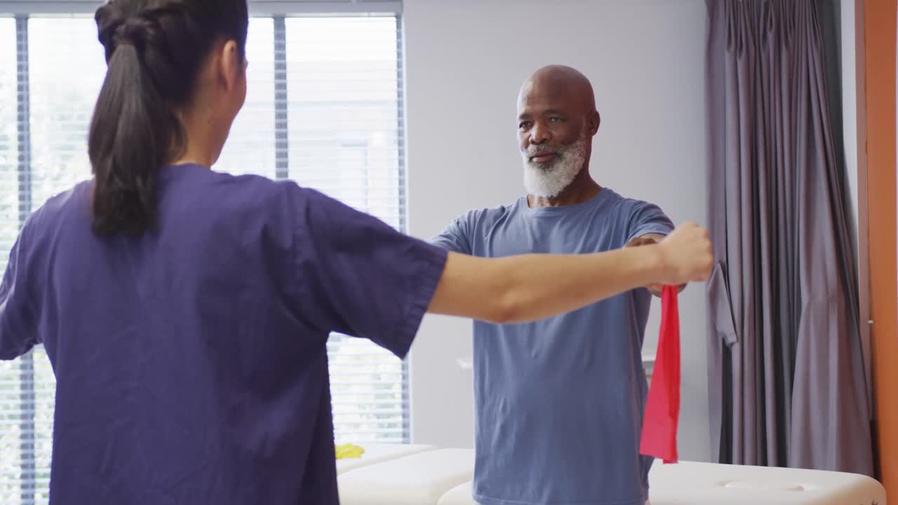 Diverse female physiotherapist and happy senior male patient in physical therapy session at hospital