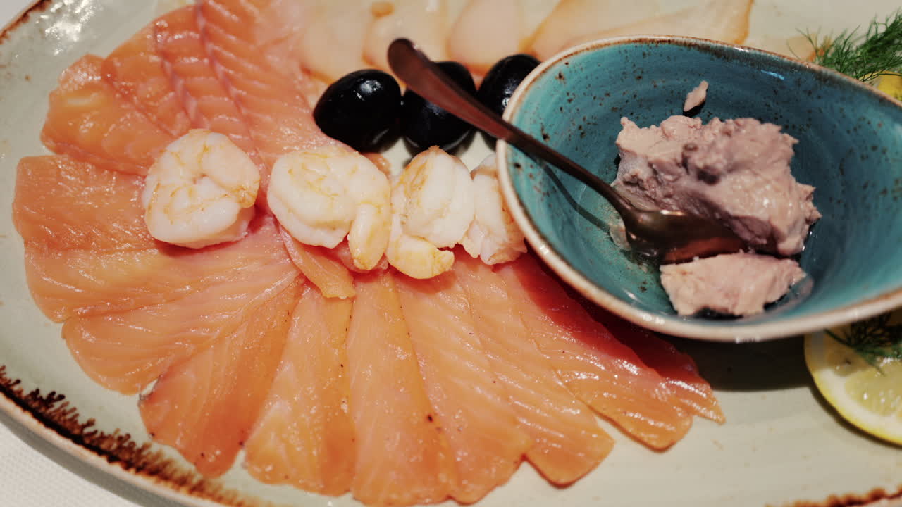 Fresh seafood platter with smoked salmon slices, shrimp, olives, and pate served with lemon and dill garnish