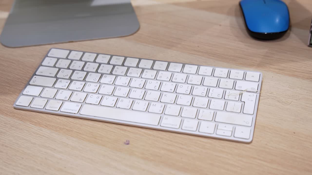 Close-up view of a wireless bilingual computer keyboard on a wooden desk beside a mouse in an indoor office workspace, highlighting modern desktop technology and everyday typing setup