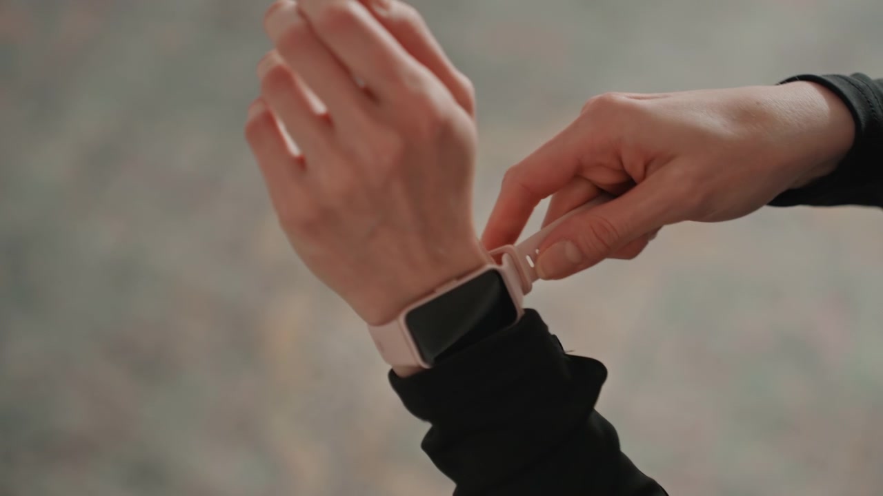 Kaukasisk kvinne fester smartklokke hjemme og forbereder seg på trening, nærbilde av håndledd og rosa reim mens trener sjekker passform og tidtaker, myk stuebakgrunn, fokusert oppvarmingsstemning.