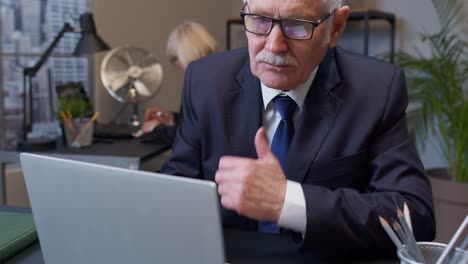 un hombre de negocios de alto rango en un traje se sienta en su escritorio, escribiendo en una computadora portátil y mirando concentrado