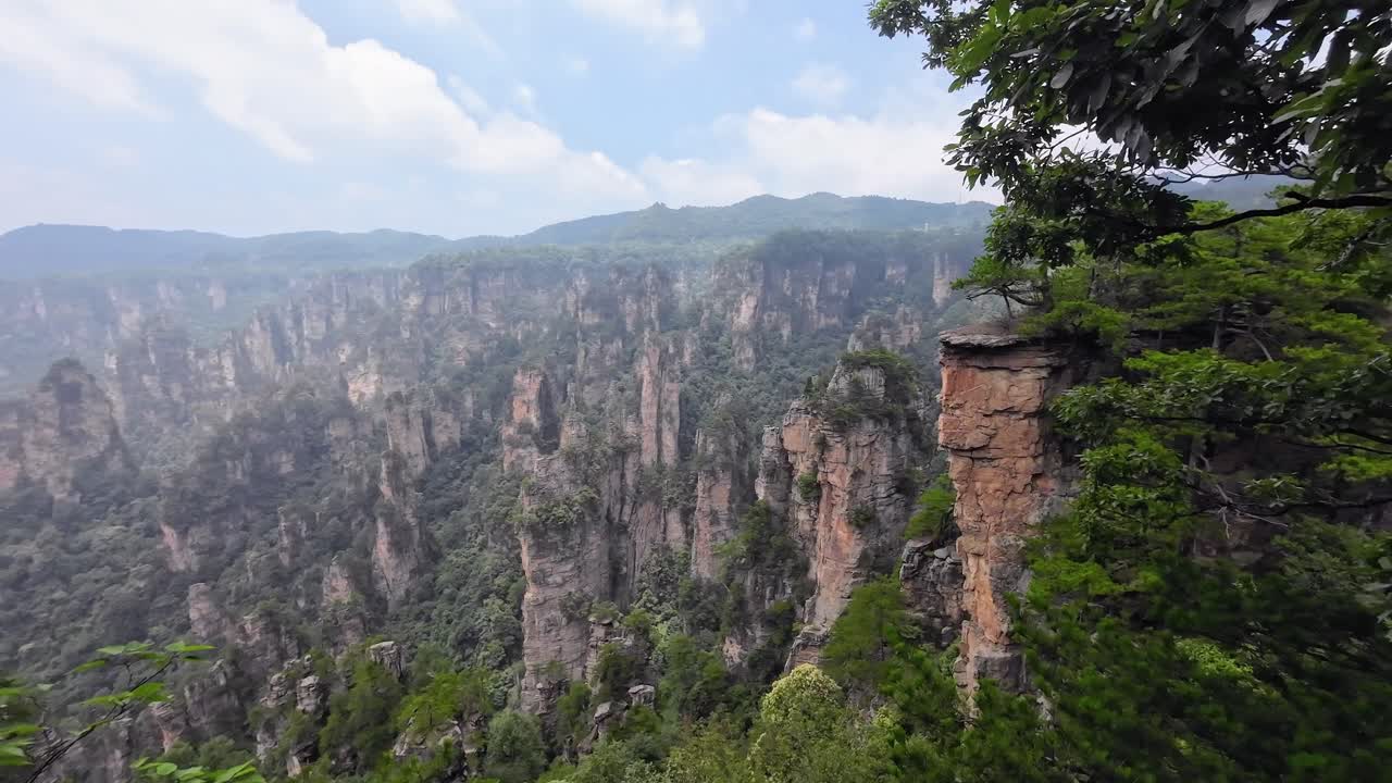 Camera slowly tilting downward between vertical cliffs and lush treetops with blue sky above