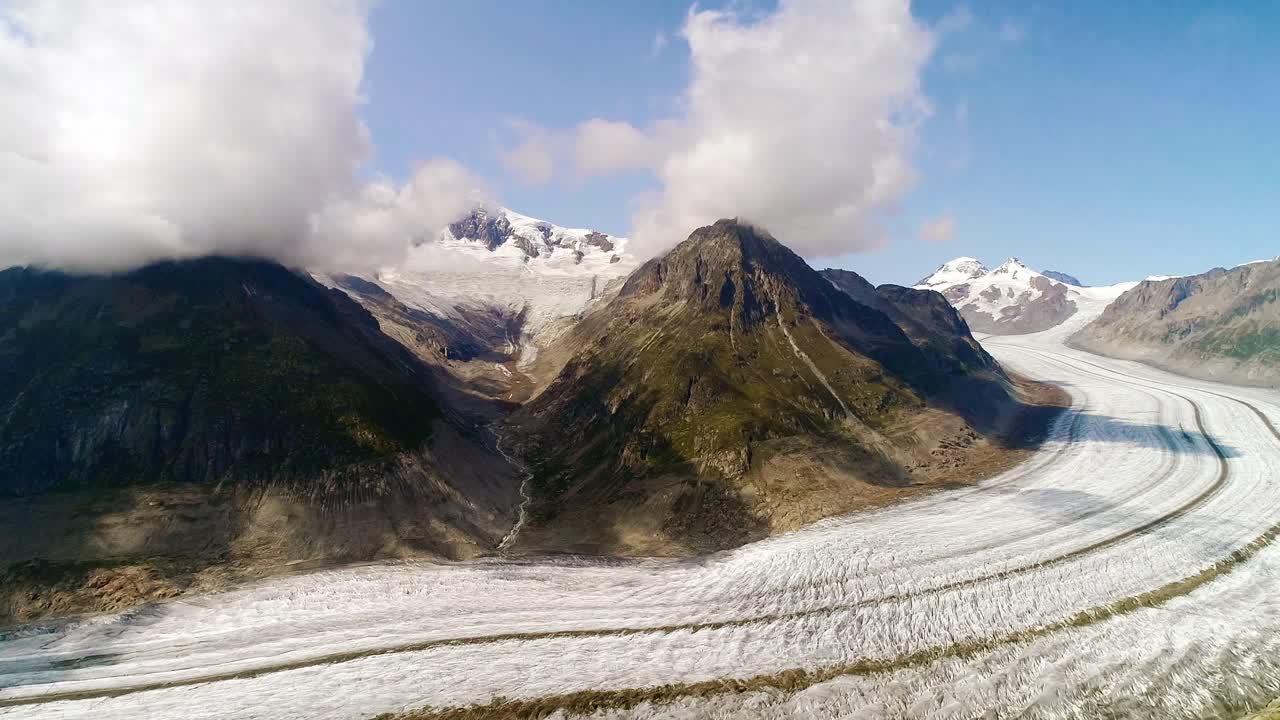 Europe largest glacier curves through Alpine terrain, cloudy bright summer sky