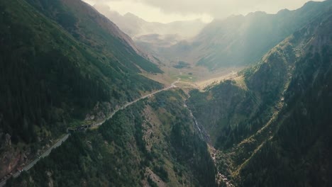 Vertical-panning-down-drone-shot-while-drone-flying-backwards,-of-a-mountain-road-next-to-a-cliff