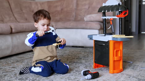 boy playing with toy tools on the floor. a young boy engages in a creative play session with a toy workbench, using tools and concentrating on his activity