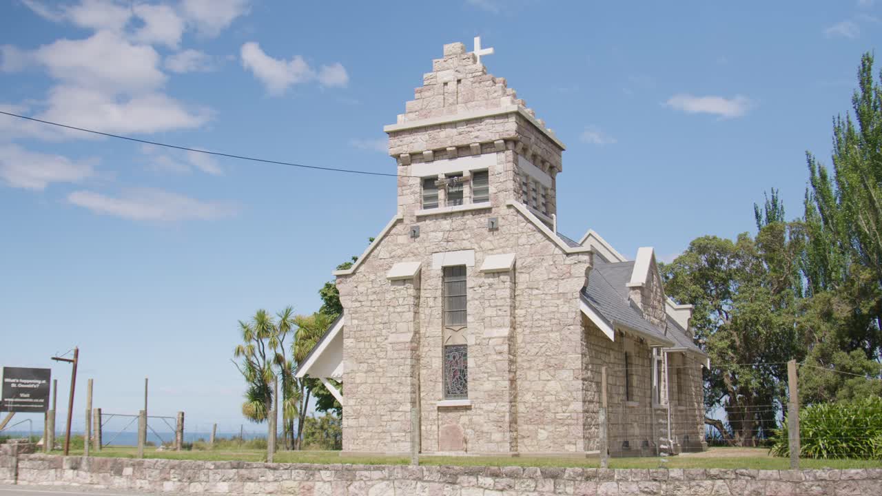 Low angle view of Saint Oswald's church in Wharanui, New Zealand with cars driving past on a clear, sunny day