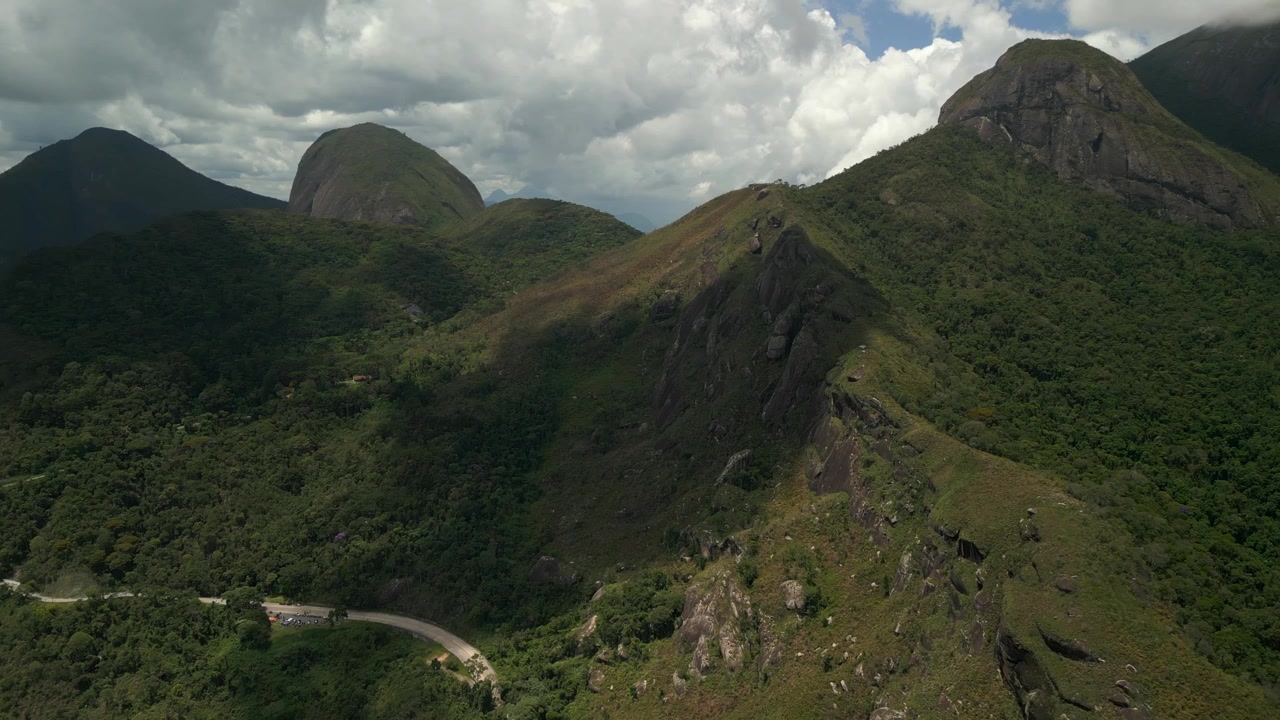 Carretera de paso de montaña rodeada de picos de bosque tropical alrededor de Petrópolis bajo una dramática mezcla de sol y nubes. Órbita de dron aérea, grabado en 4K a 25 fps.