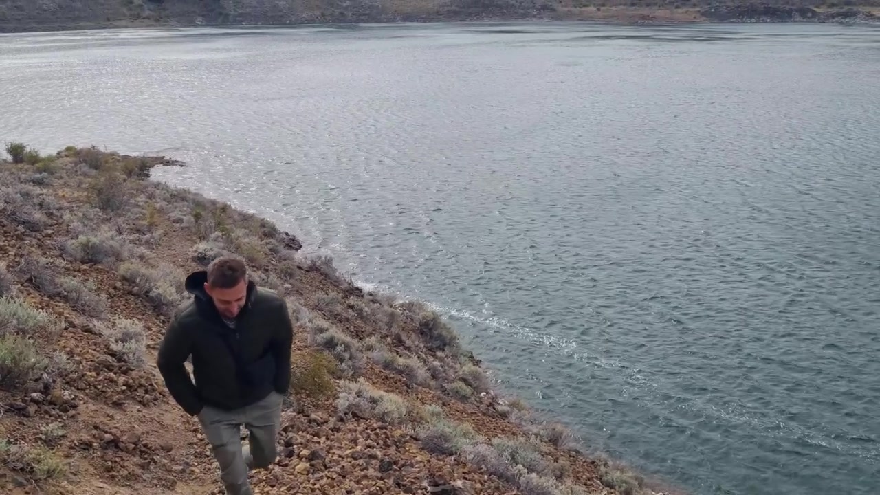 Un turista solitario esplora le rive vulcaniche della Laguna Azul vicino a Río Gallegos, Argentina. Cieli tempestosi circondano questo lago vulcanico nel campo vulcanico di Pali Aike, mettendo in mostra il paesaggio selvaggio della Patagonia.