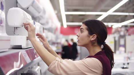 young brunette girl checking out sewing mashine in hardware store. costumer buying home appliance. choosing household equipment.