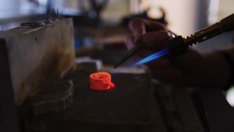 close up of female jeweller working on ring in studio using blowtorch