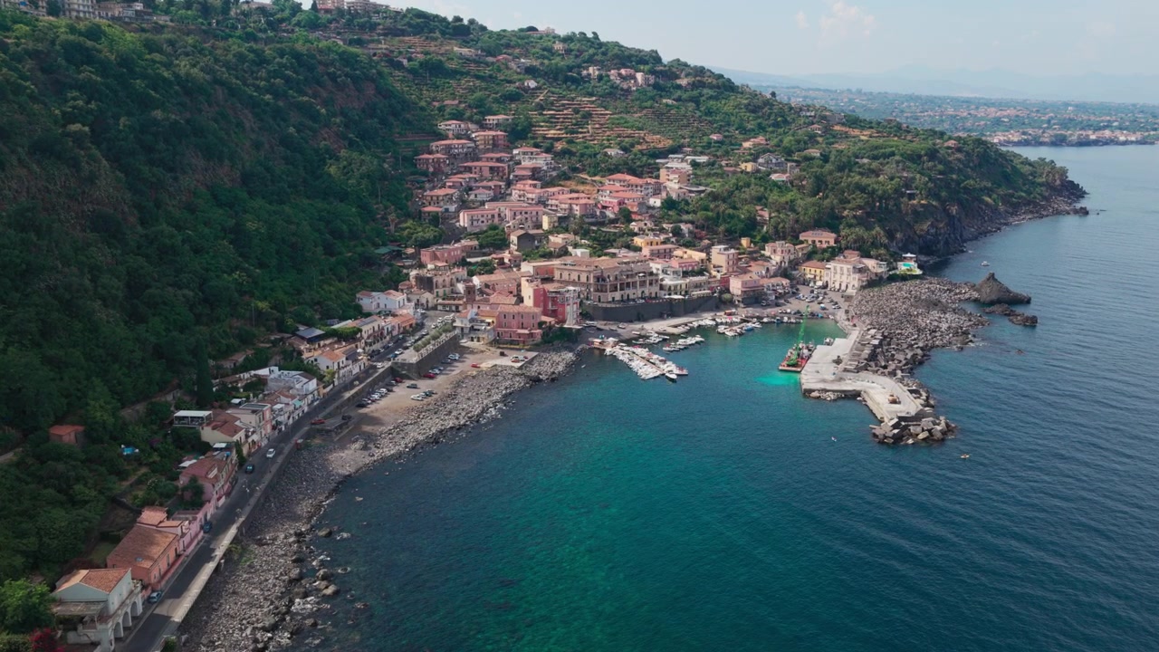 Ampia veduta aerea al tramonto di Santa Maria la Scala, un villaggio di pescatori con acqua blu e scogliere di lava basaltica vicino al Monte Etna ad Acireale, Catania, Sicilia, Italia, una destinazione popolare sulla costa ionica.